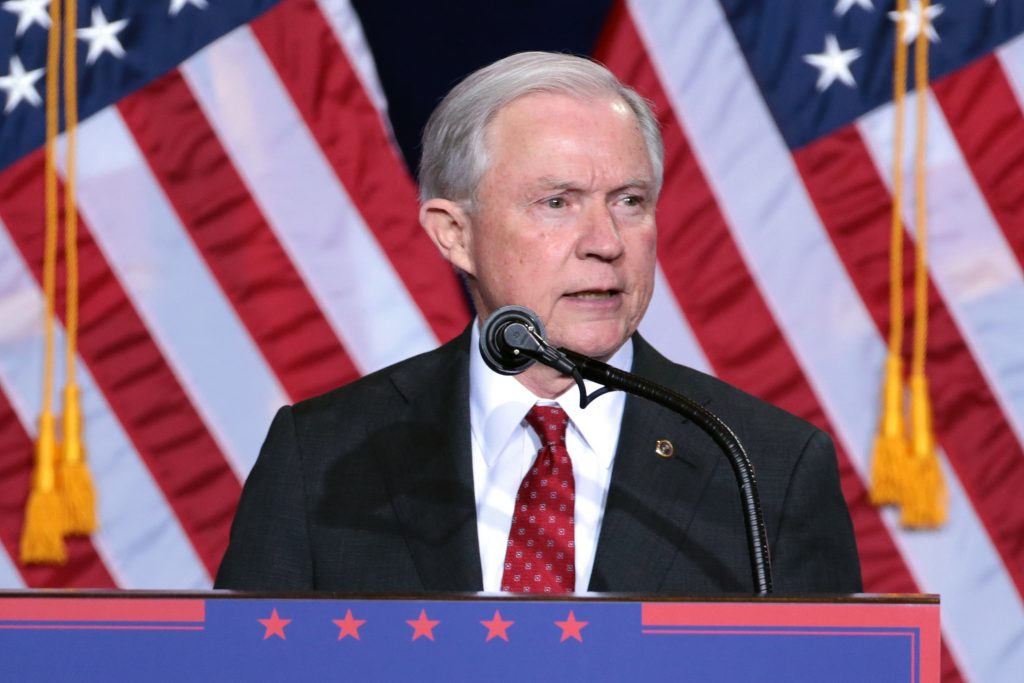 Jeff Sessions speaking in front of American flags